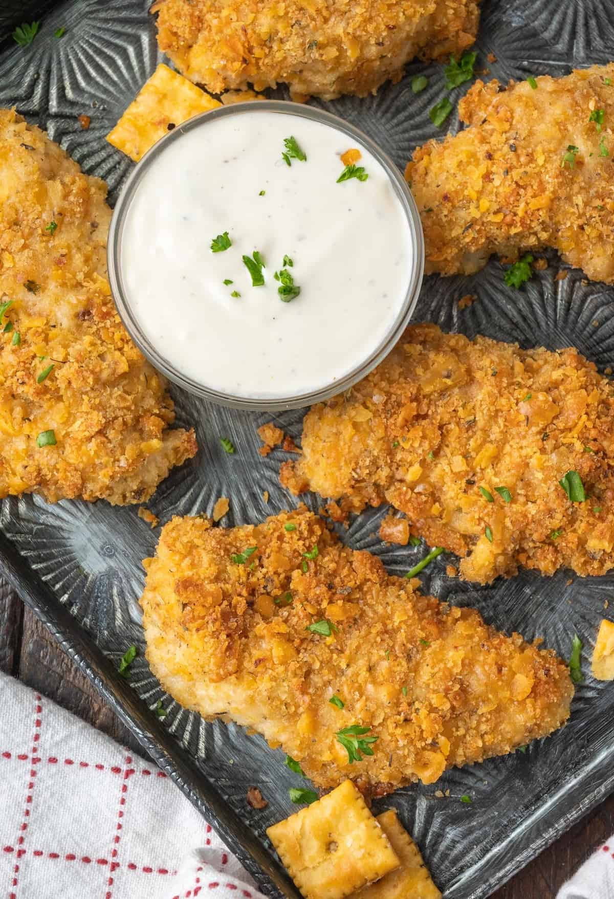 Cheez it chicken tenders on a baking sheet with ranch dressing.