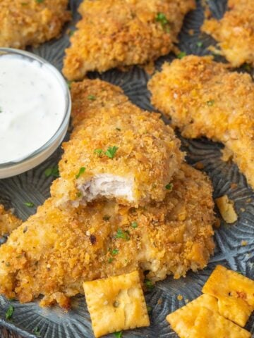 Chicken tenders on a baking sheet with ranch dressing and a bite out of one.