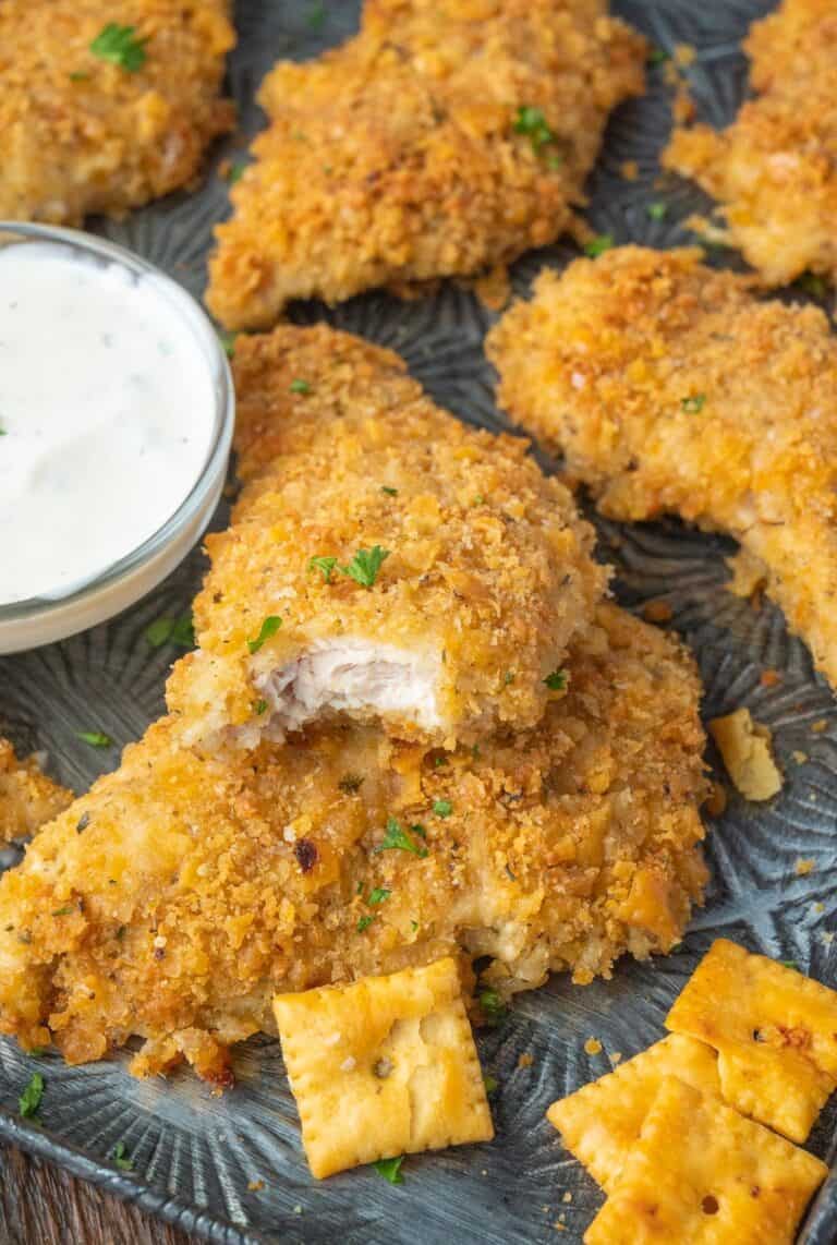 Chicken tenders on a baking sheet with ranch dressing and a bite out of one.