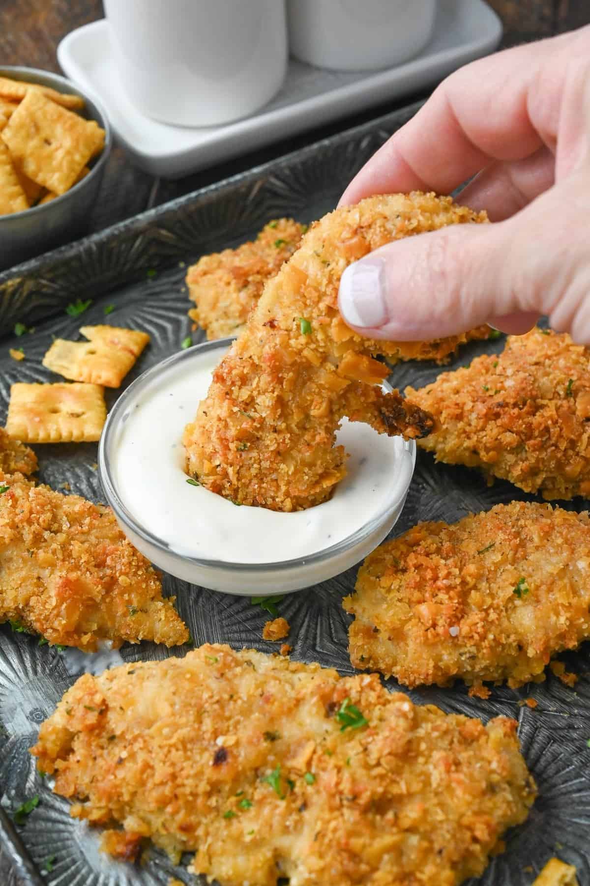 Cheez it chicken tender being dipped into ranch dressing.