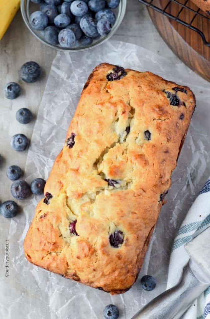 Banana Blueberry cream cheese bread on a cutting board with blueberries and bananas