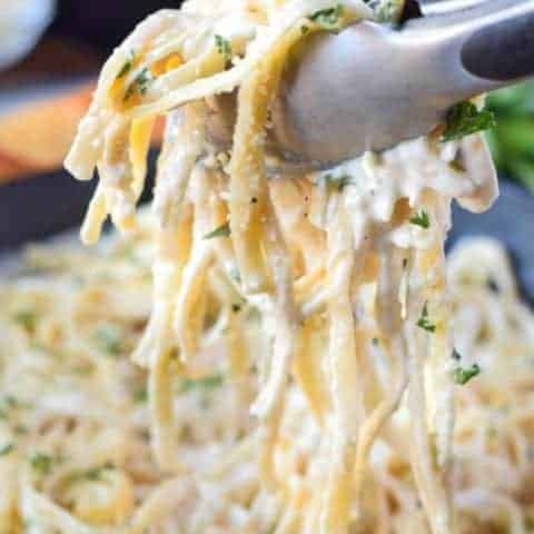 garlic fettuccine alfredo in a cast iron skillet with tongs picking up a scoop