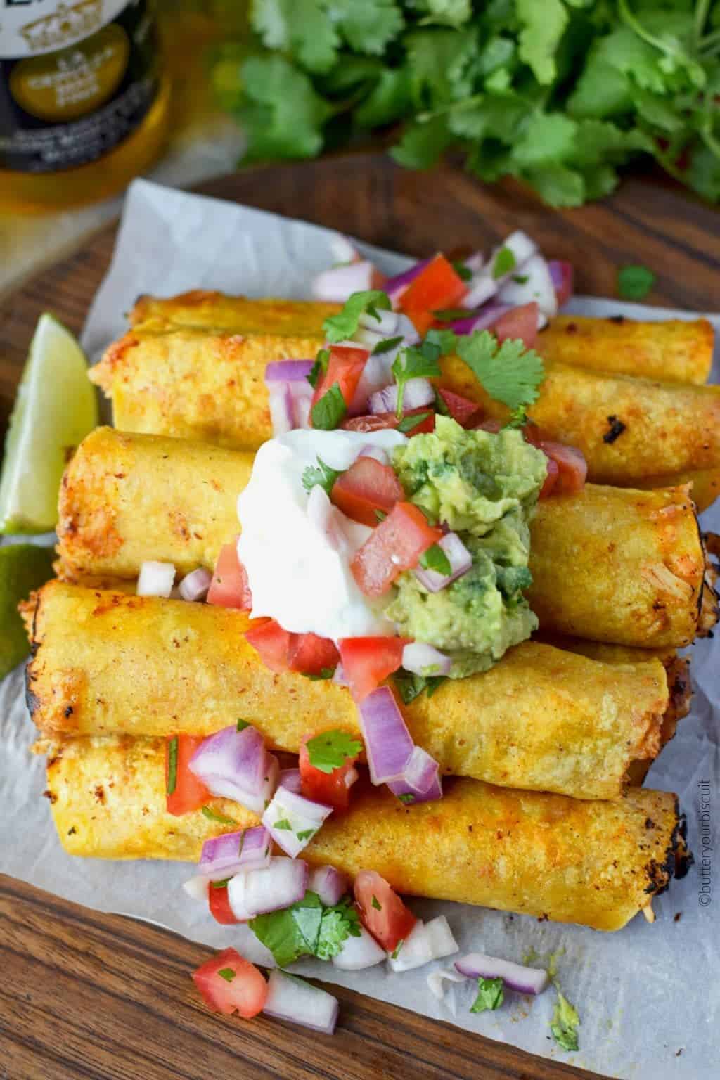 A plate of chicken taquitos with sour cream and guacamole.