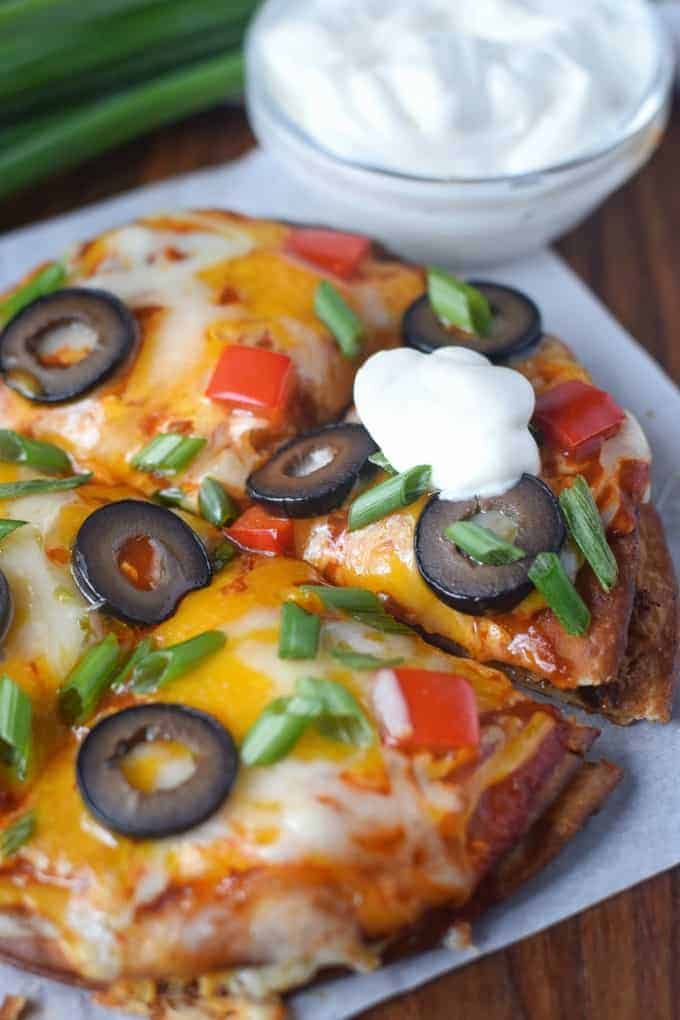 A Mexican pizza cut into fourths and a dollop of sour cream on one piece.