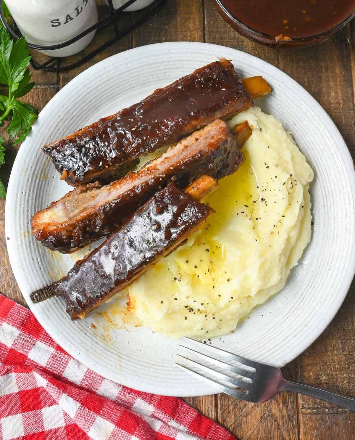 Three ribs on a plate with a side of mashed potatoes.