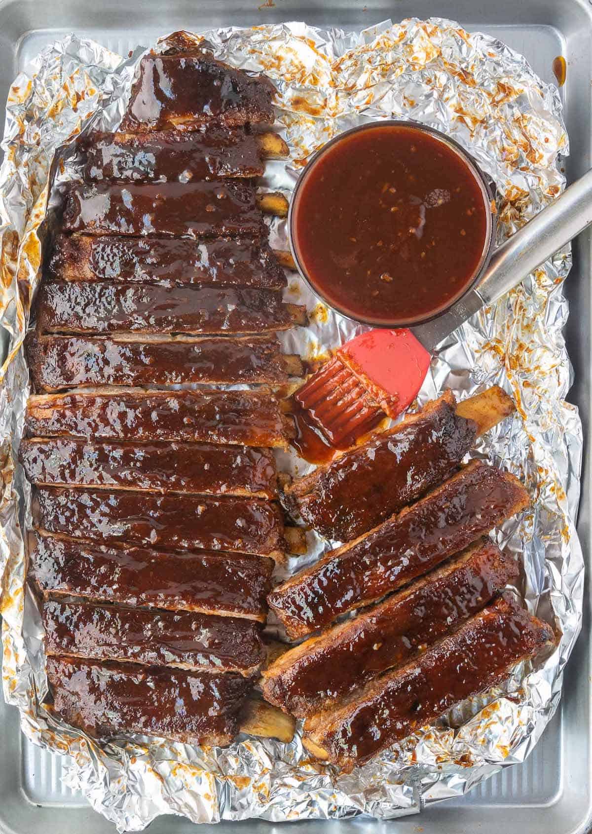 Baked ribs on foil with a side of bbq sauce.