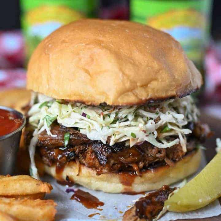 Slow cooker pulled pork sandwich with chipotle slaw. On a serving plate with a dill pickle, fries and a side of ketchup.