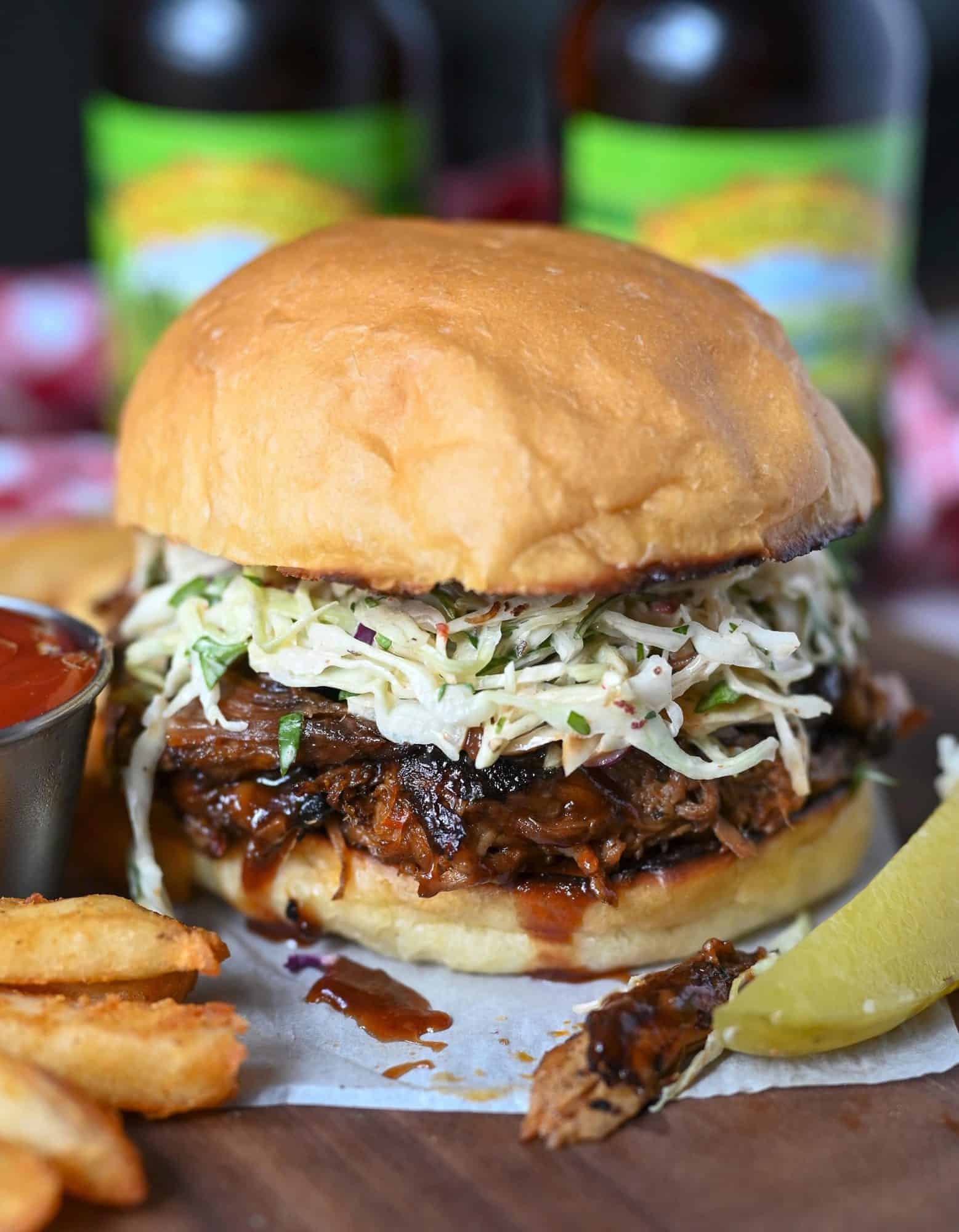 Slow cooker pulled pork sandwich with chipotle slaw. On a serving plate with a dill pickle, fries and a side of ketchup.