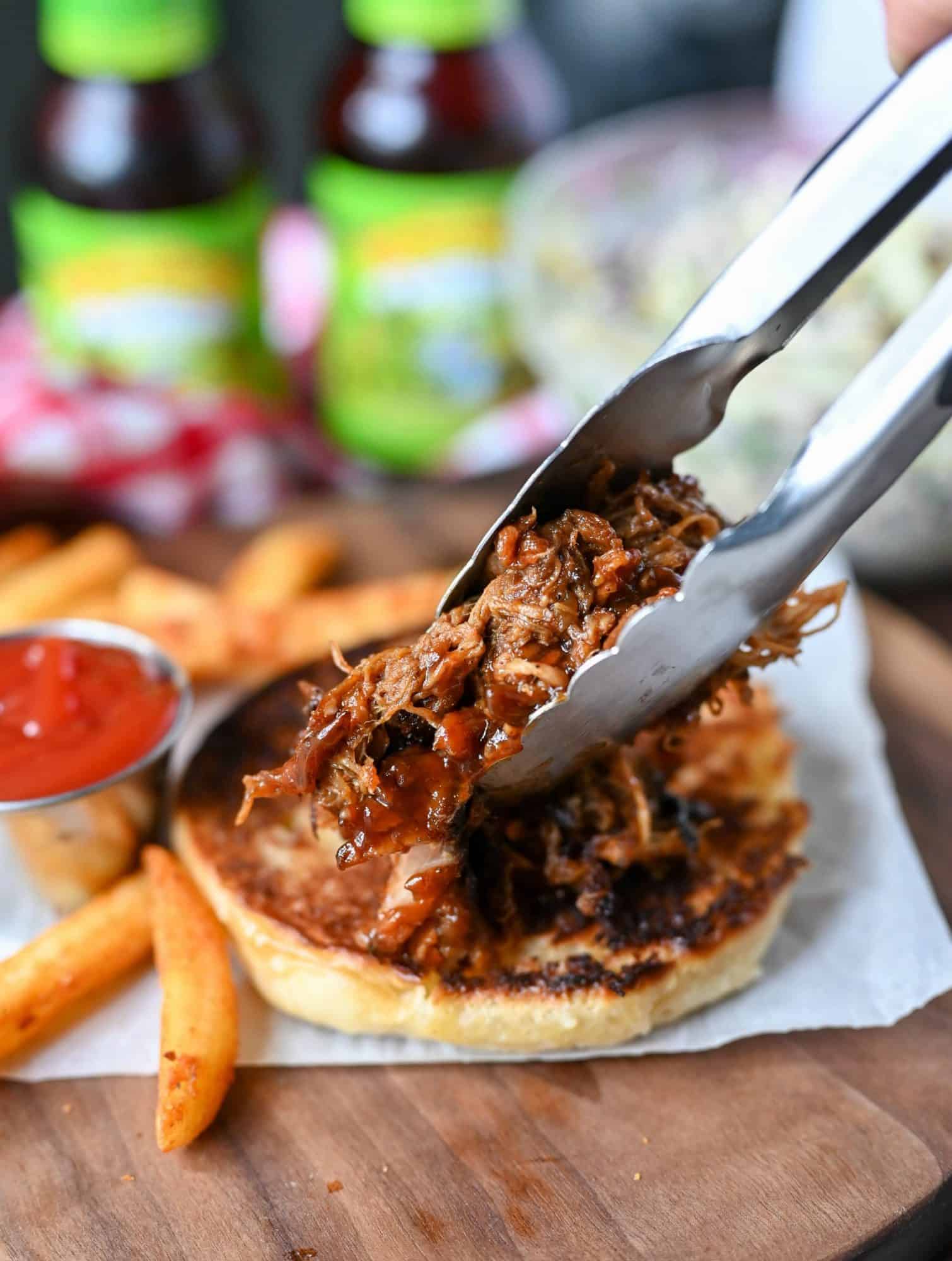 slow cooker pork placed on bottom toasted bun with tongs.