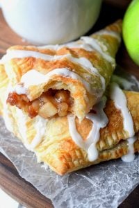 apple turnovers with glaze drizzle over top and a white coffee cup and green apple