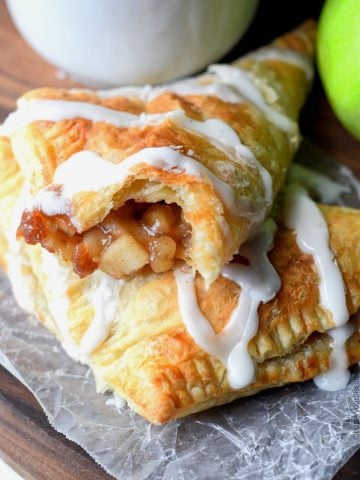 apple turnovers with glaze drizzle over top and a white coffee cup and green apple