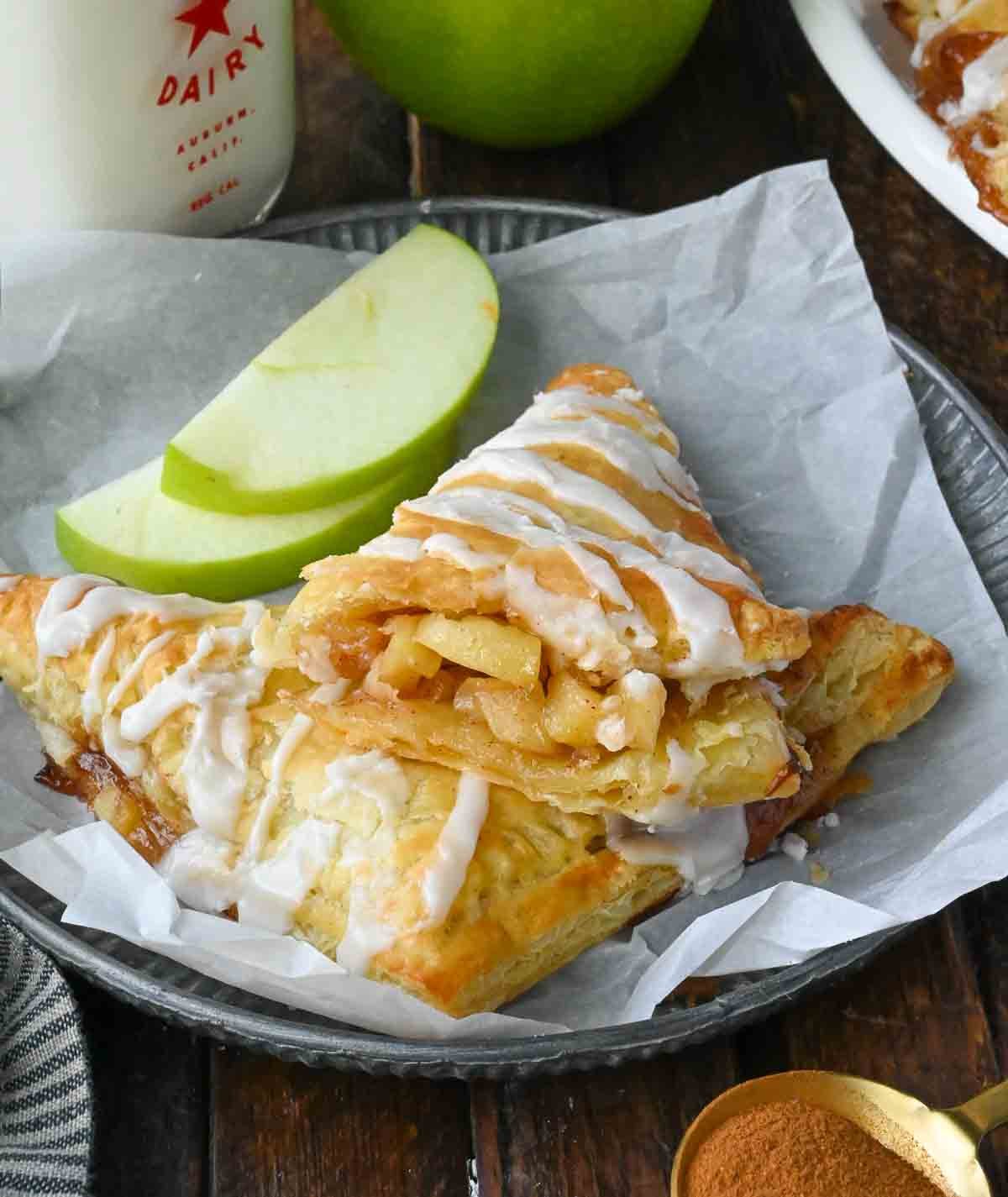 Apple pie turnovers on a plate with sliced apples.