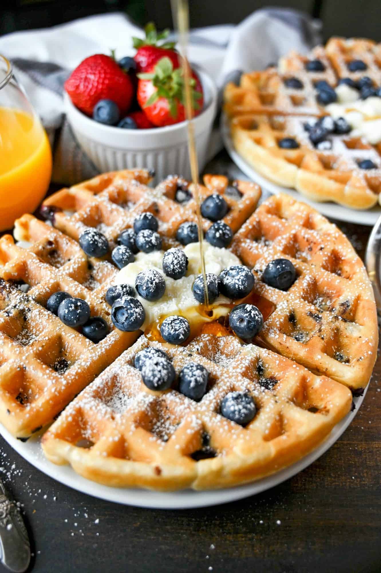 Blueberry waffle on a plate with warm maple syrup being poured on top.