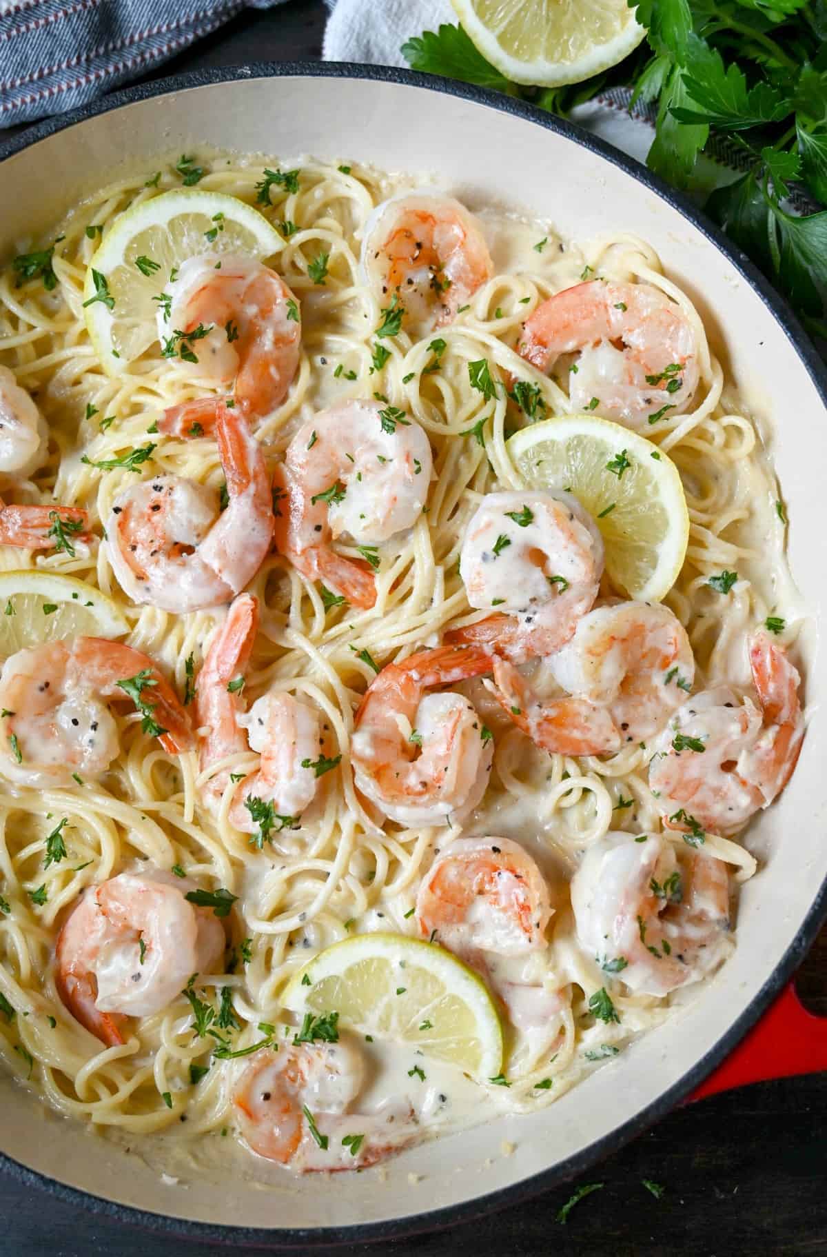 Shrimp pasta in a cast iron red dish with lemon slices and fresh parsley on top.