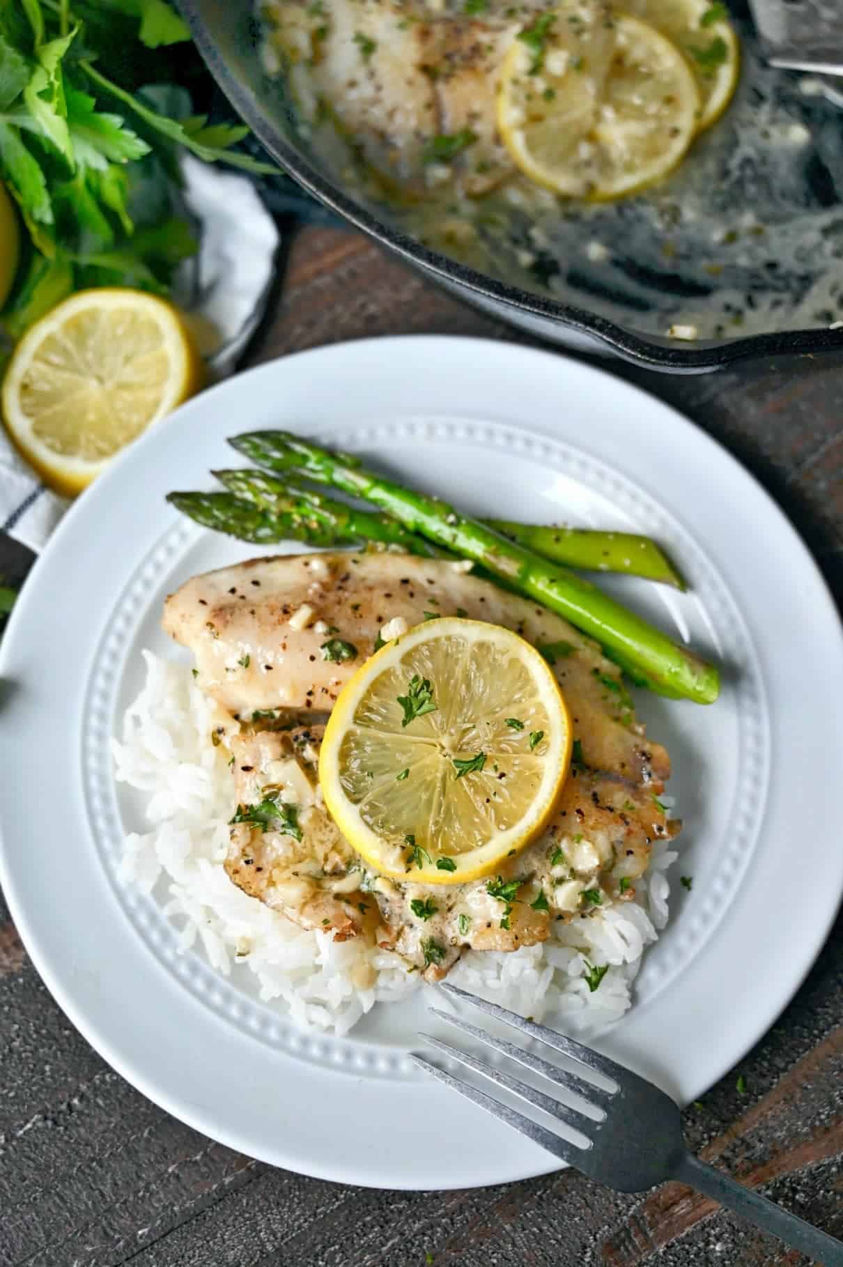 Pan seared tilapia on a bed of white rice with roasted asparagus on the side.