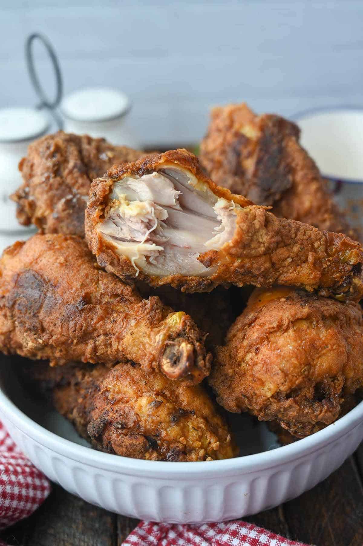 A bowl full of spicy fried chicken legs with a bite out of one.
