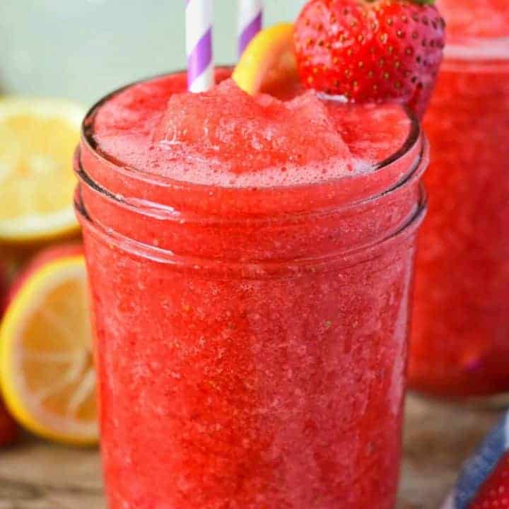 strawberry lemonade vodka slush in a glass with a strawberry and lemon slice