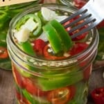 A jar of pickled jalapenos with a fork pulling one out.