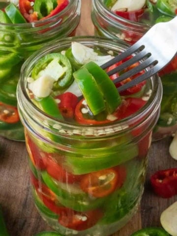 A jar of pickled jalapenos with a fork removing one.
