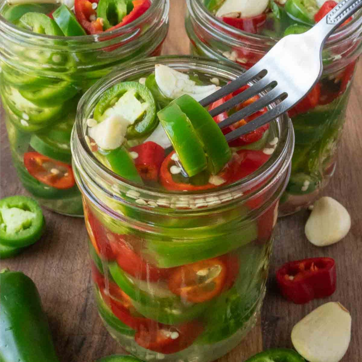 A jar of pickled jalapenos with a fork removing one.