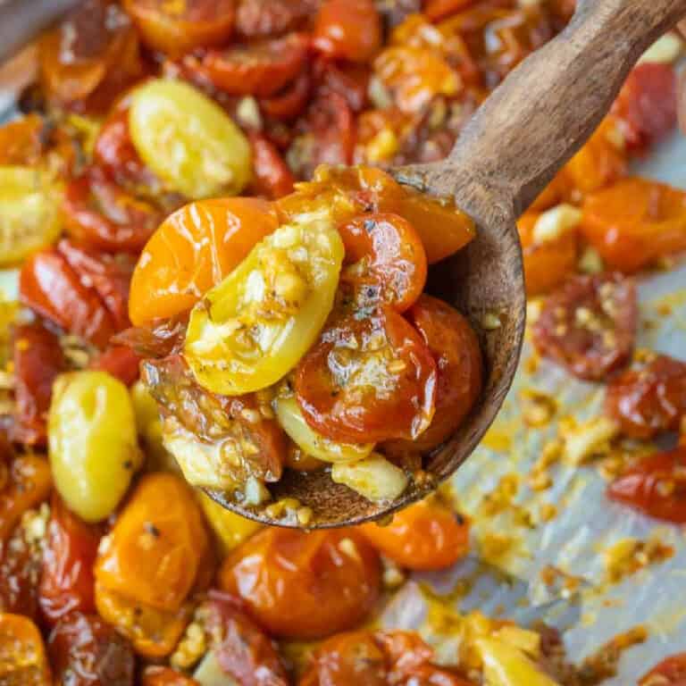 A wooden spoon picking up some roasted tomatoes.