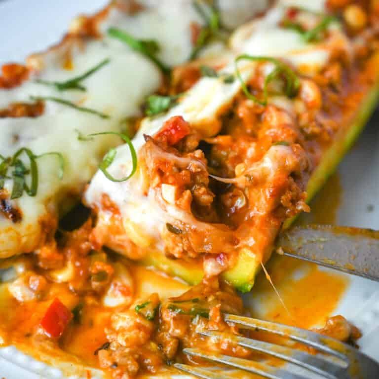 Zucchini stuffed with Italian sausage miTwo Italian sausage stuffed zucchini on a white plate and a bite removed from one.