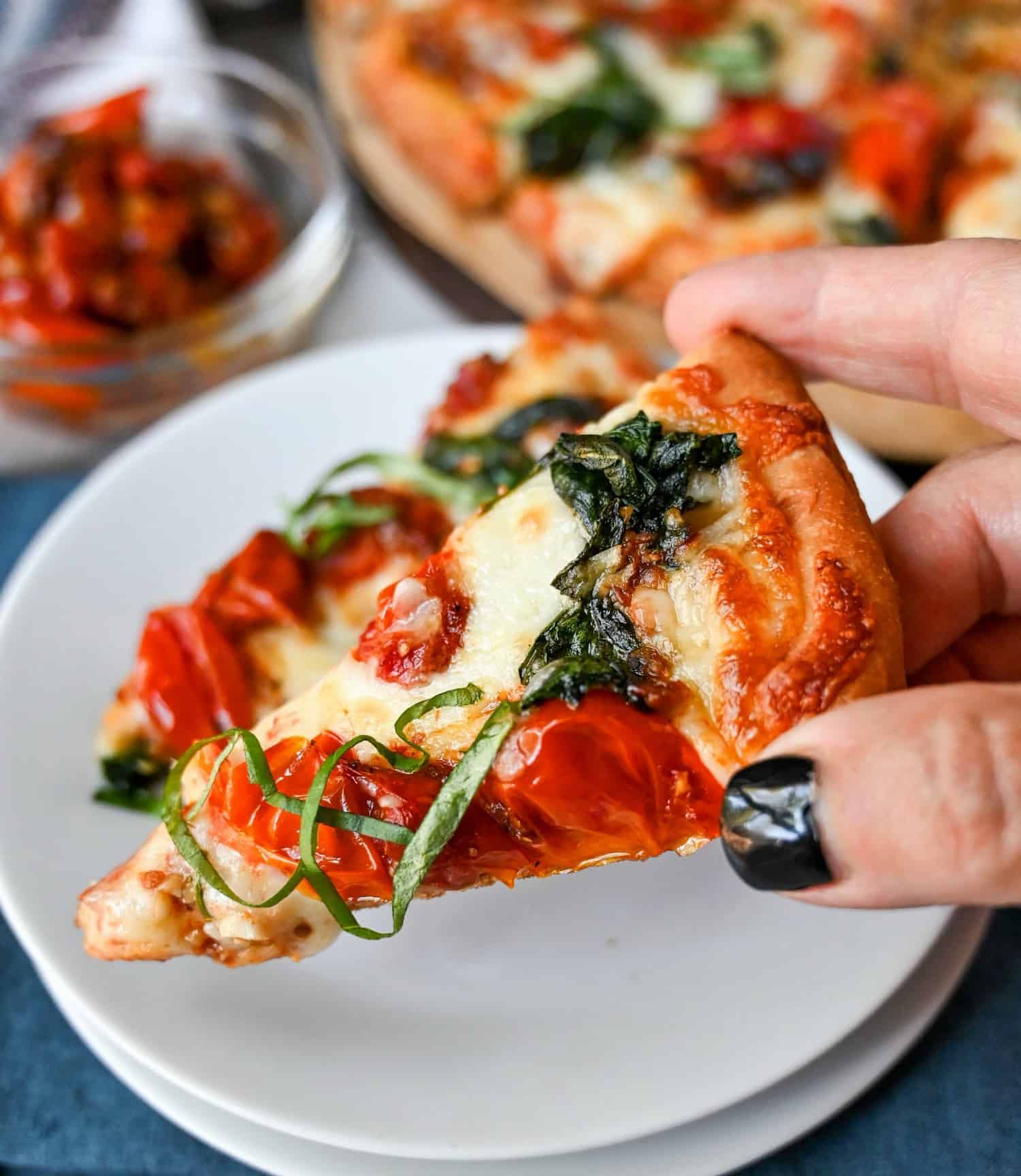 A slice of roasted tomato spinach flatbread being picked up from a small white plate.