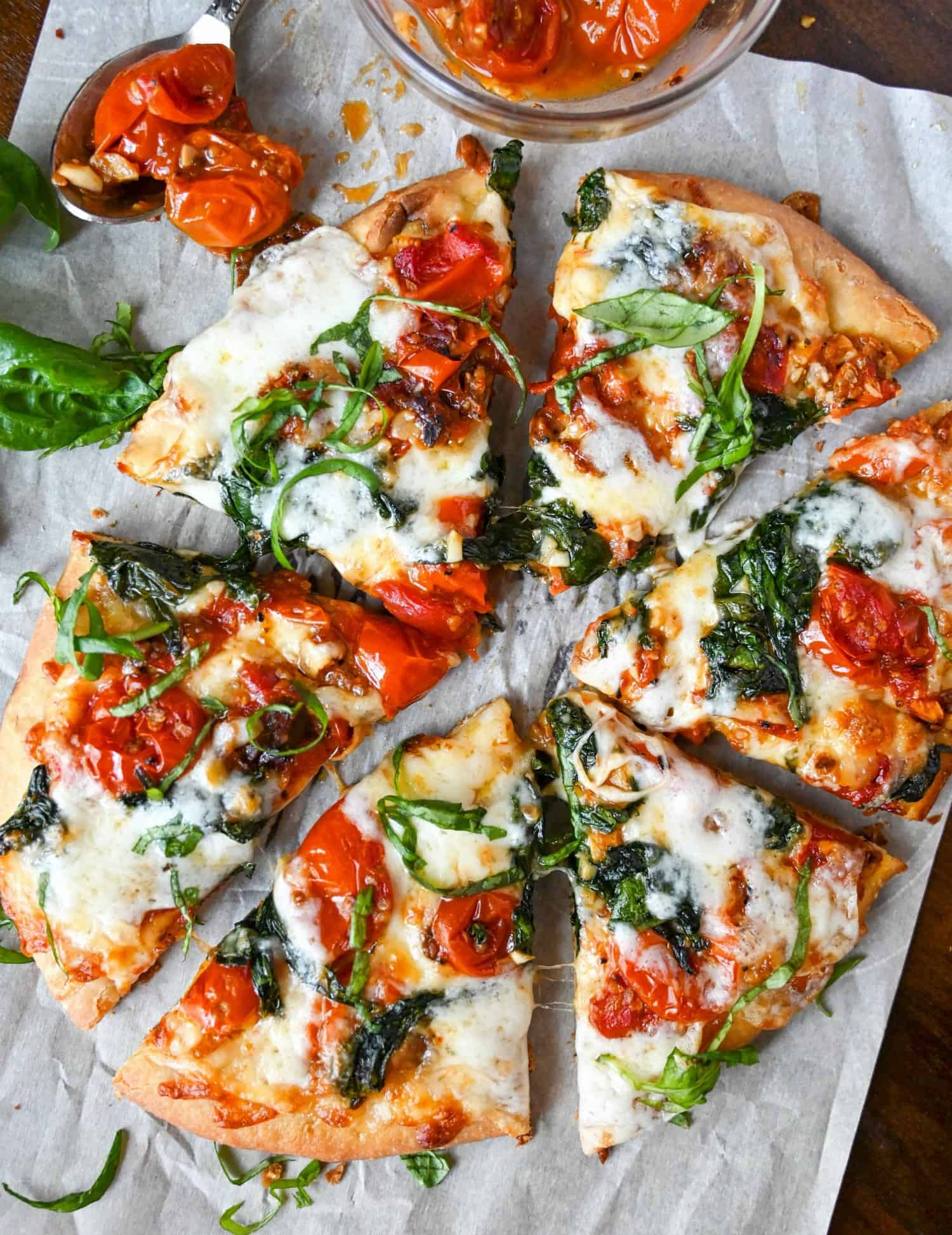 Flaybread cut into six slices on a piece of parchment paper, with a small bowl of roasted cherry tomatoes on the side.