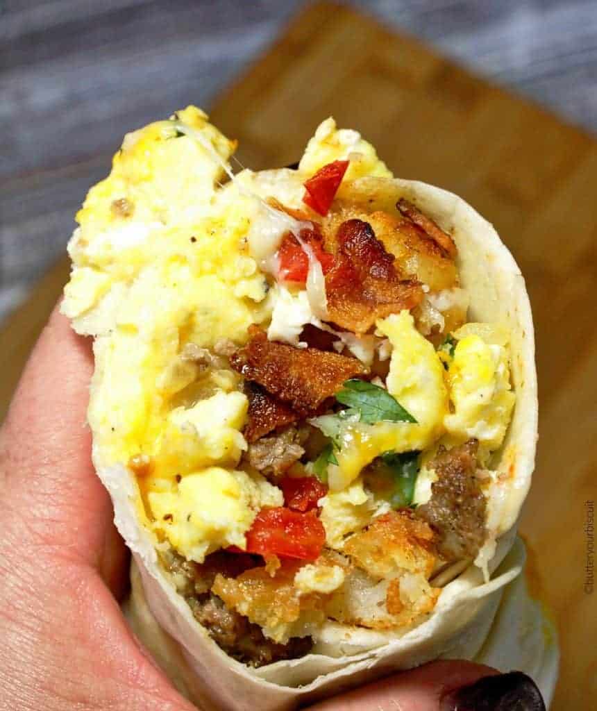 A close up of a person holding a piece of food, with Breakfast burrito