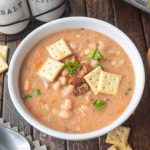 Bean soup in a bowl with bacon and saltine crackers on top.