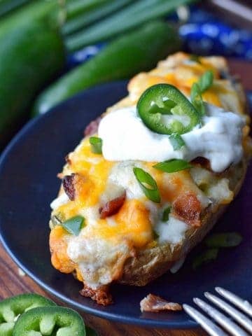 bacon jalapeno twice baked potato on a black plate with sour cream and a jalapeno slice on top