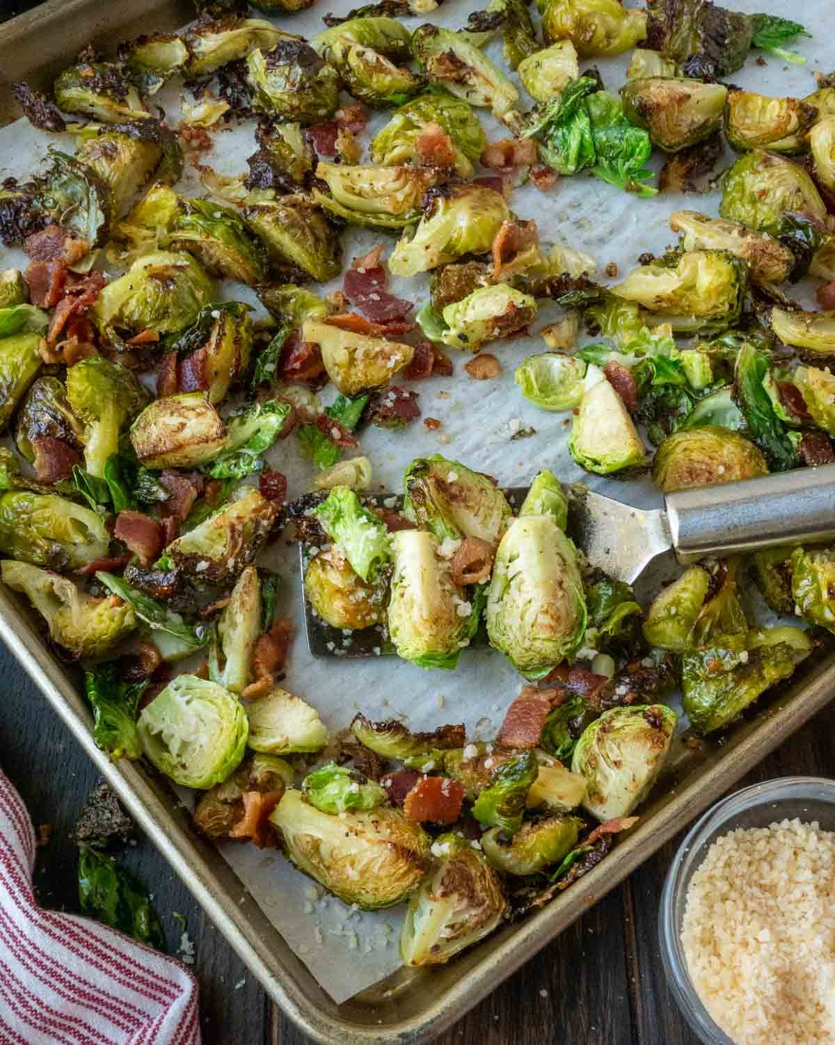 Roasted brussels sprouts on a baking sheet with a spatula.