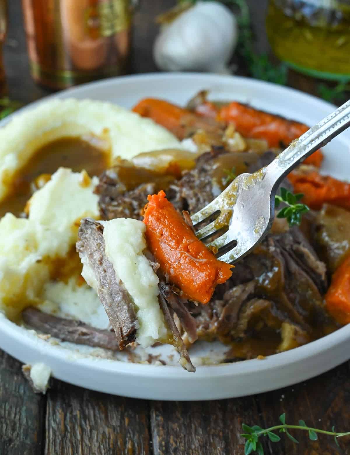 Slow cooker pot roasr with carrots and mashed potatoes on a white plate.