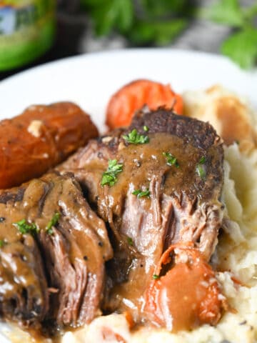 Pot roast on a white plate with mashed potatoes and roasted carrots,