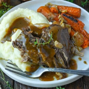 Pot roast with gravy, mashed potatoes and carrots on a plate.
