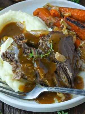 Pot roast with gravy, mashed potatoes and carrots on a plate.