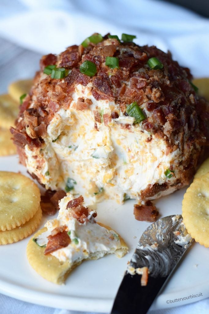 A bacon jalapeno cheese ball on a white plte with Ritz crackers on the side.