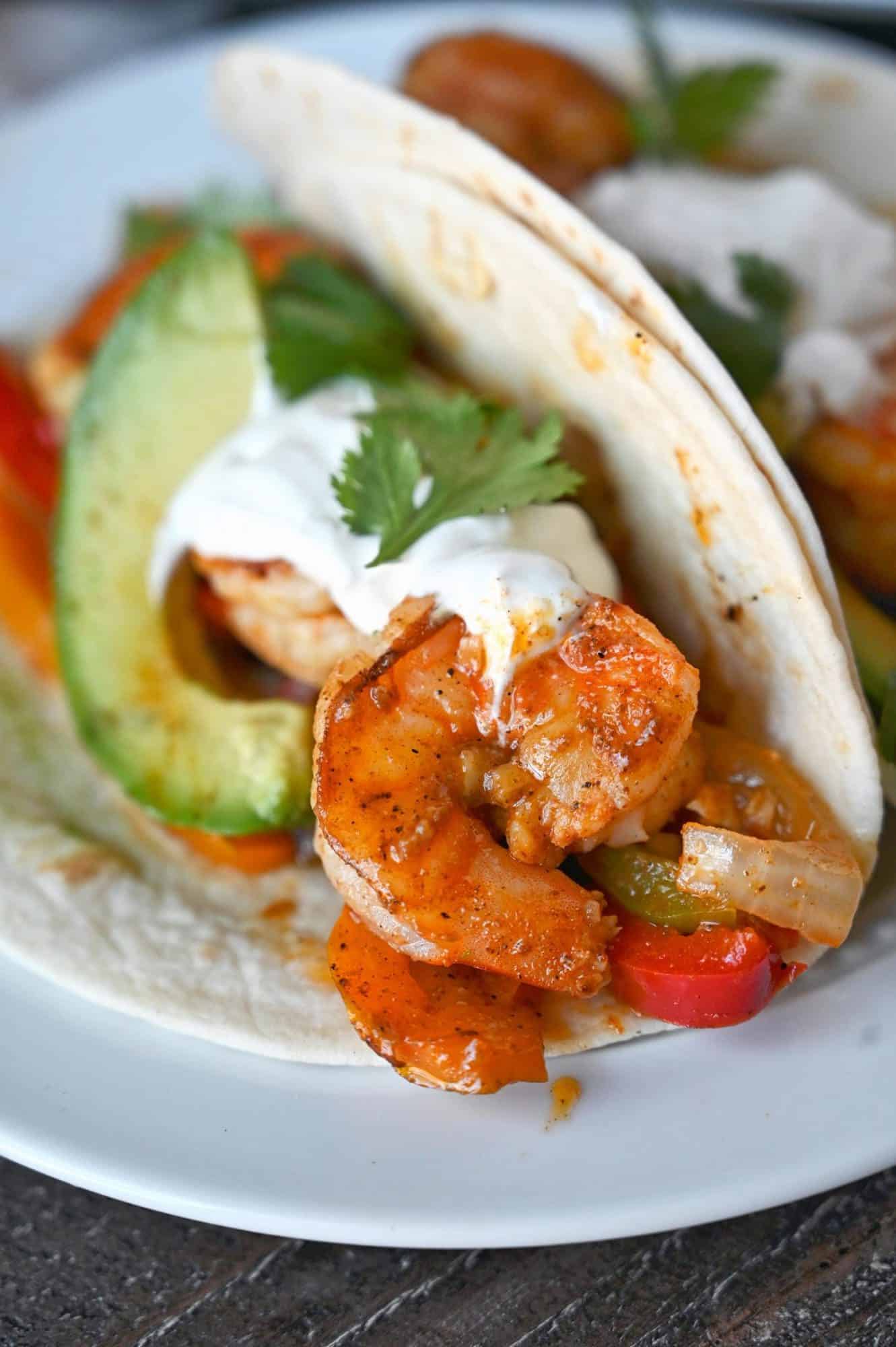 Cajun shrimp fajitas in a flour tortilla with a slice of avacado, sourcream and cilantro.
