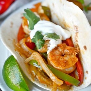 Cajun shrimp with peppers in a flour tortilla and a lime slice on the side.