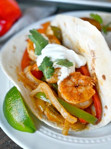 Cajun shrimp with peppers in a flour tortilla and a lime slice on the side.