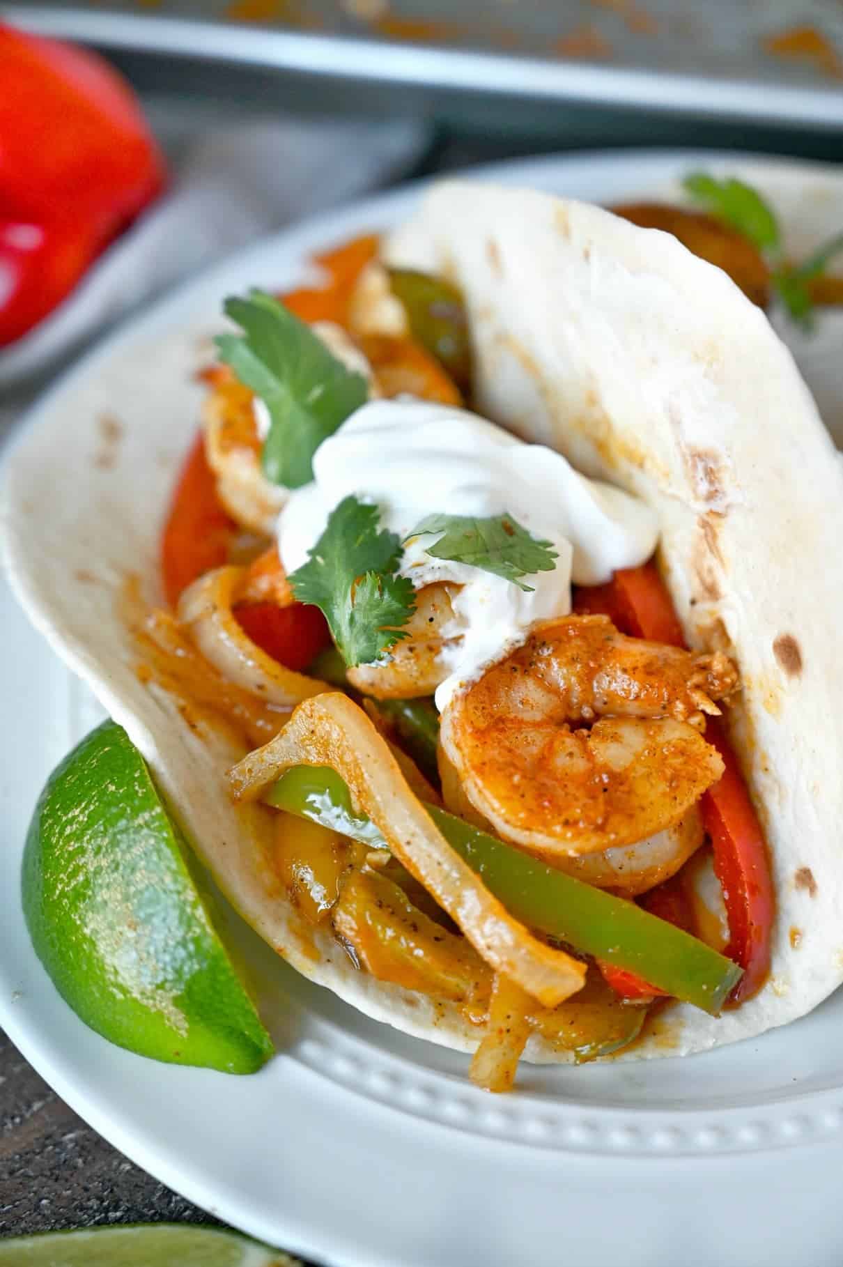 Cajun shrimp with peppers in a flour tortilla and a lime slice on the side.
