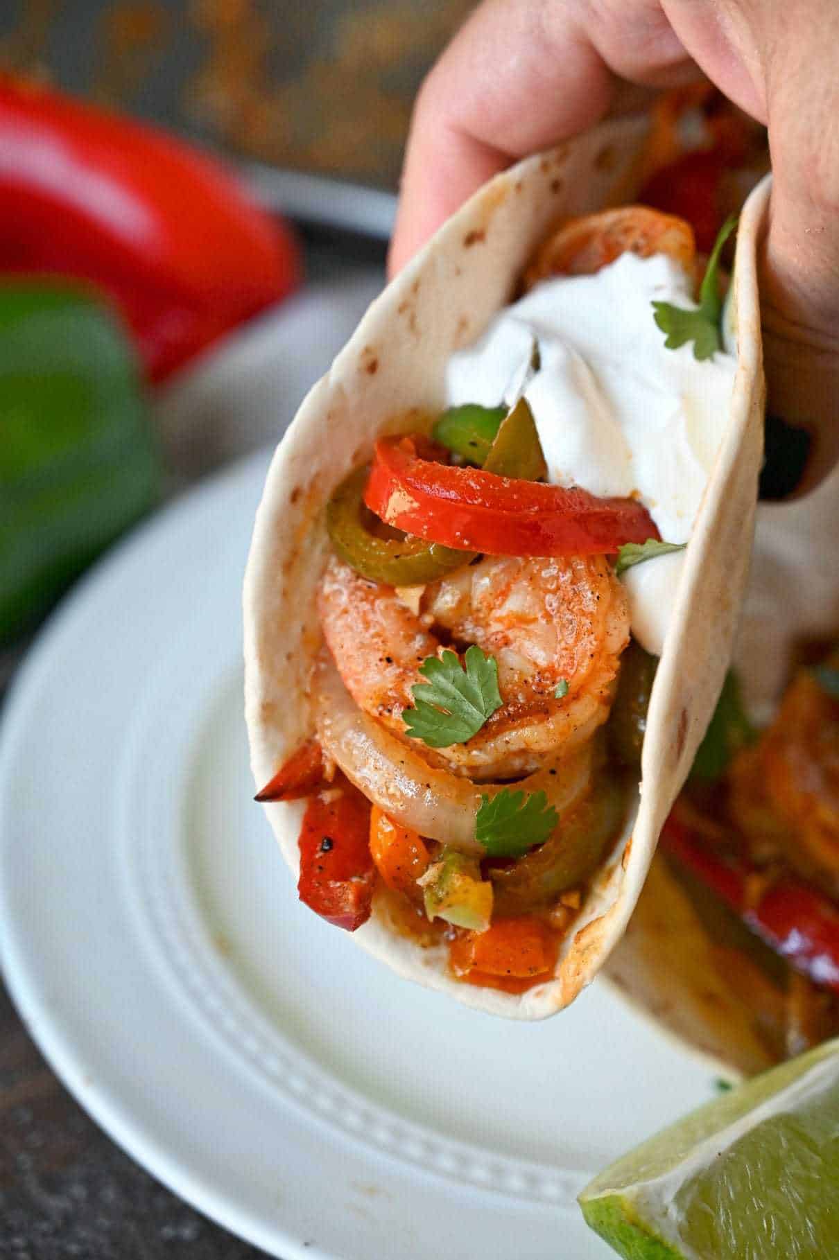 Cajun shrimo with peppers in a flour tortilla and a dallop of sour cream. Being picked up in a hand.