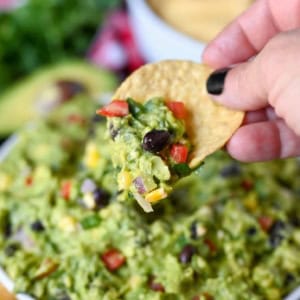 Guacamole in a white bowl with a tortilla chip scooping some out.