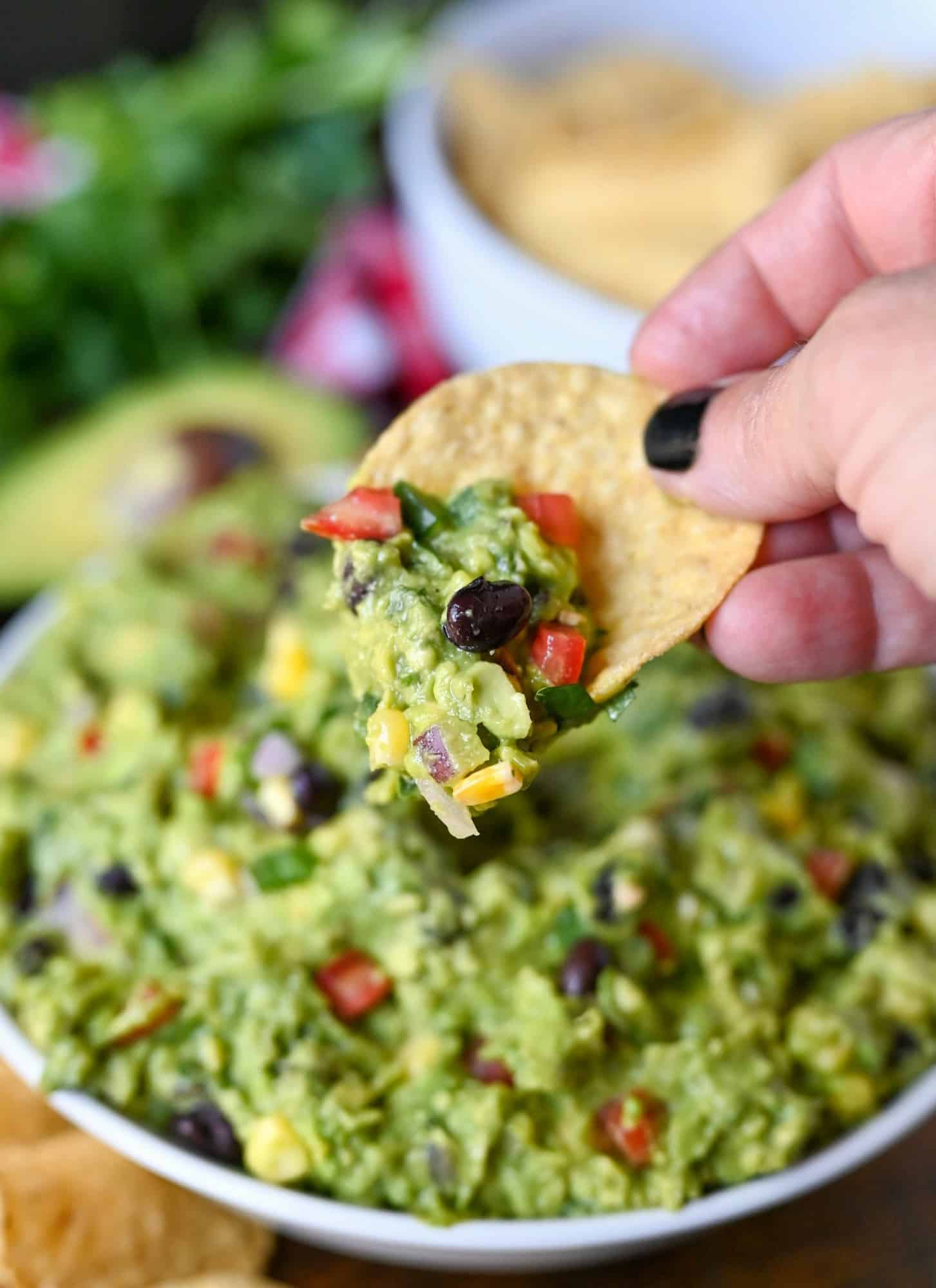 Guacamole in a white bowl with a tortilla chip scooping some out.