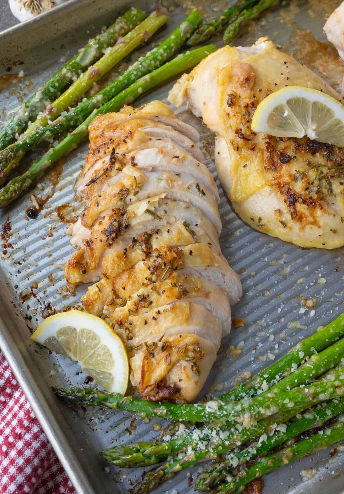 Chicken breasts with asparagus on a baking sheet.