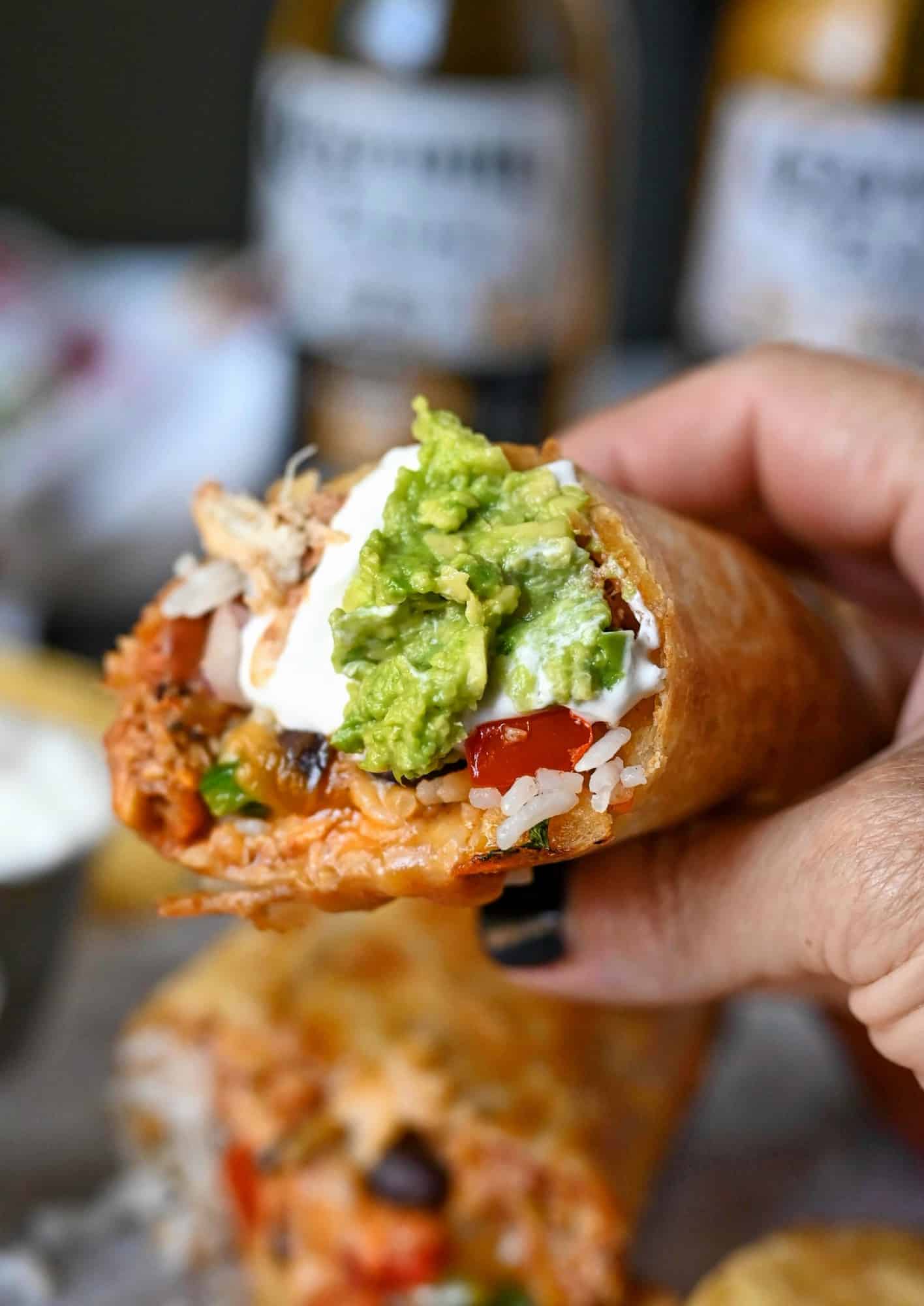 Slow cooker chicken burrito cut in half. Held in one hand with guacamole and sour cream on the end.