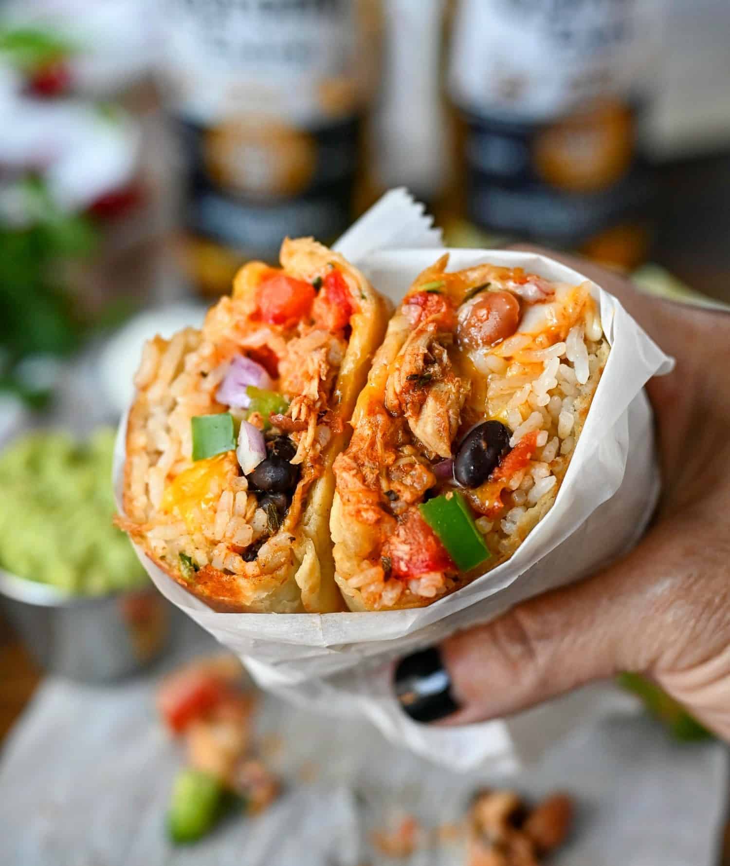 Slow cooker chicken burritos wrapped in white parchments paper held in one hand.