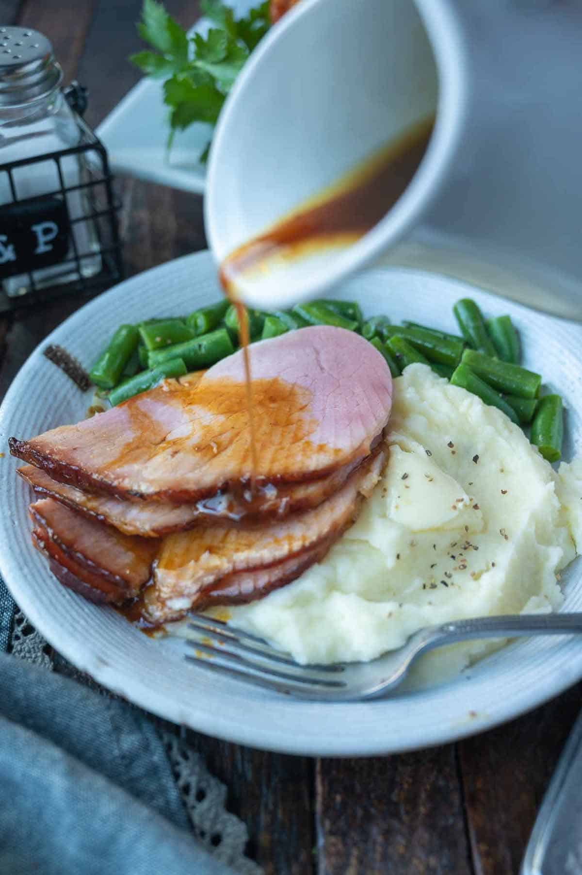 Sliced ham on a plate with mashed potatoes and green beans.