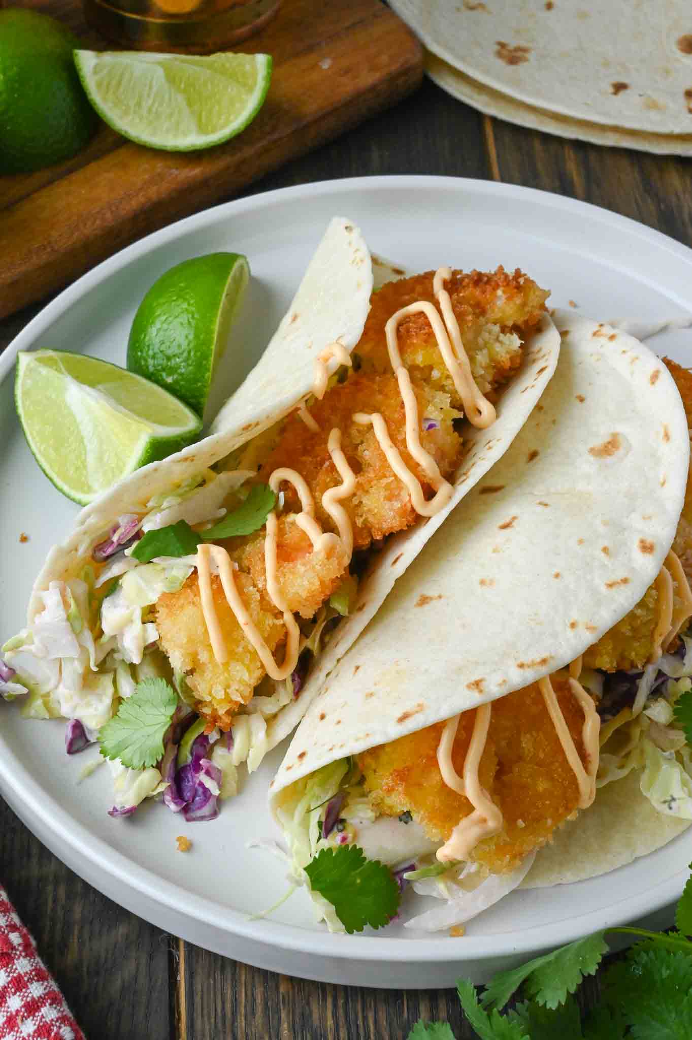 Crispy shrimp tacos on a white plate with lime slices.