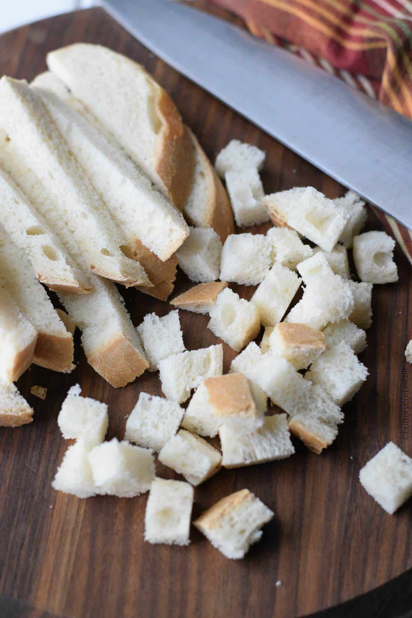 Old bread being cut into small bite sized squares.